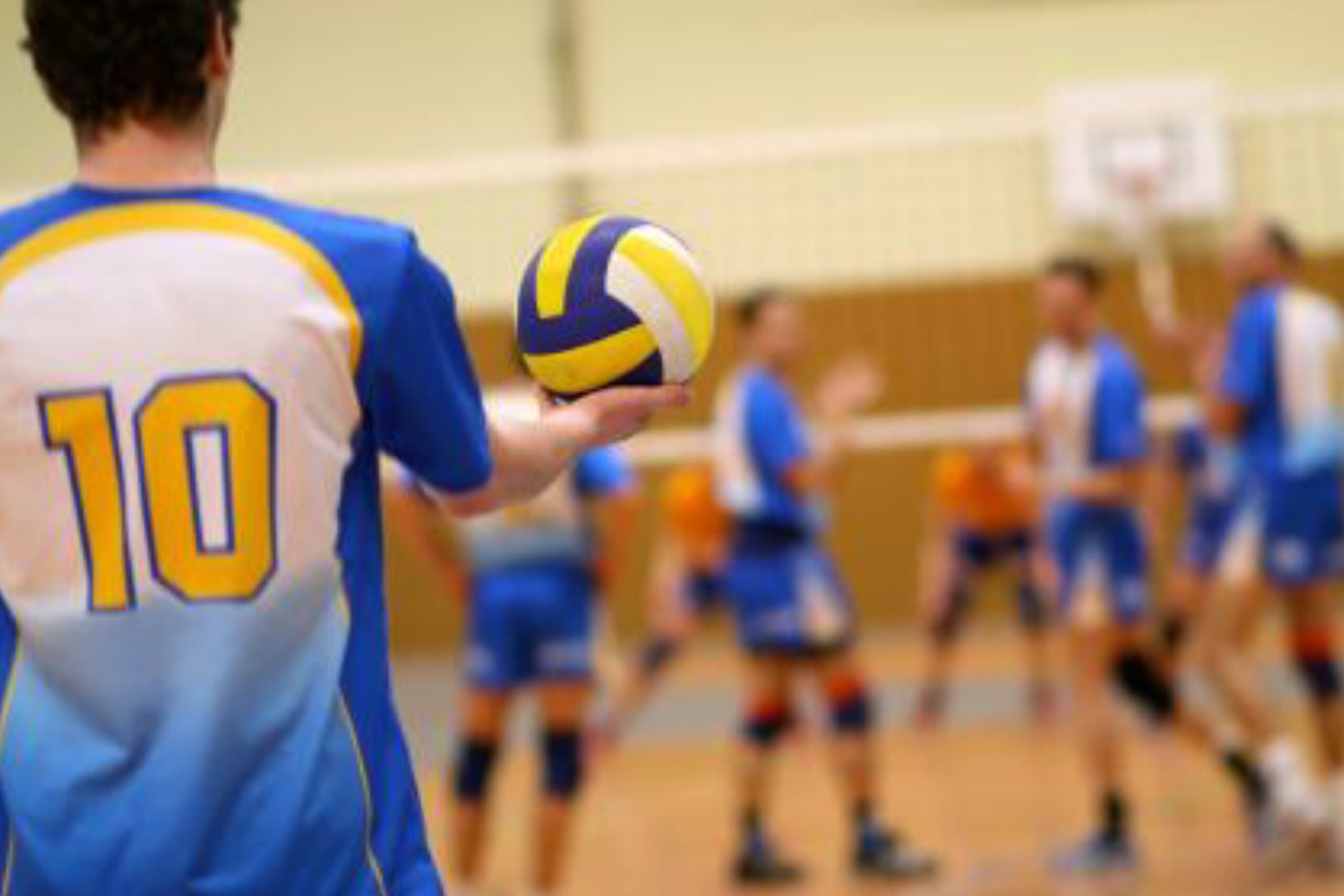 Volleyball player preparing to serve during an indoor volleyball match, with teammates ready on the court.